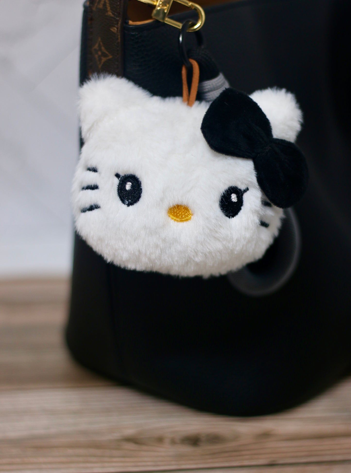 Plush keychain shaped like a cat face with a black bow on a black bag.