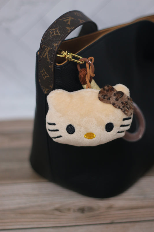 Black handbag with a Hello Kitty keychain featuring leopard print on a wooden surface.